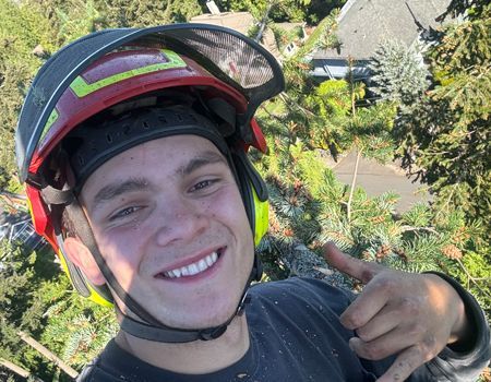 A young man wearing a helmet is smiling and pointing at the camera.