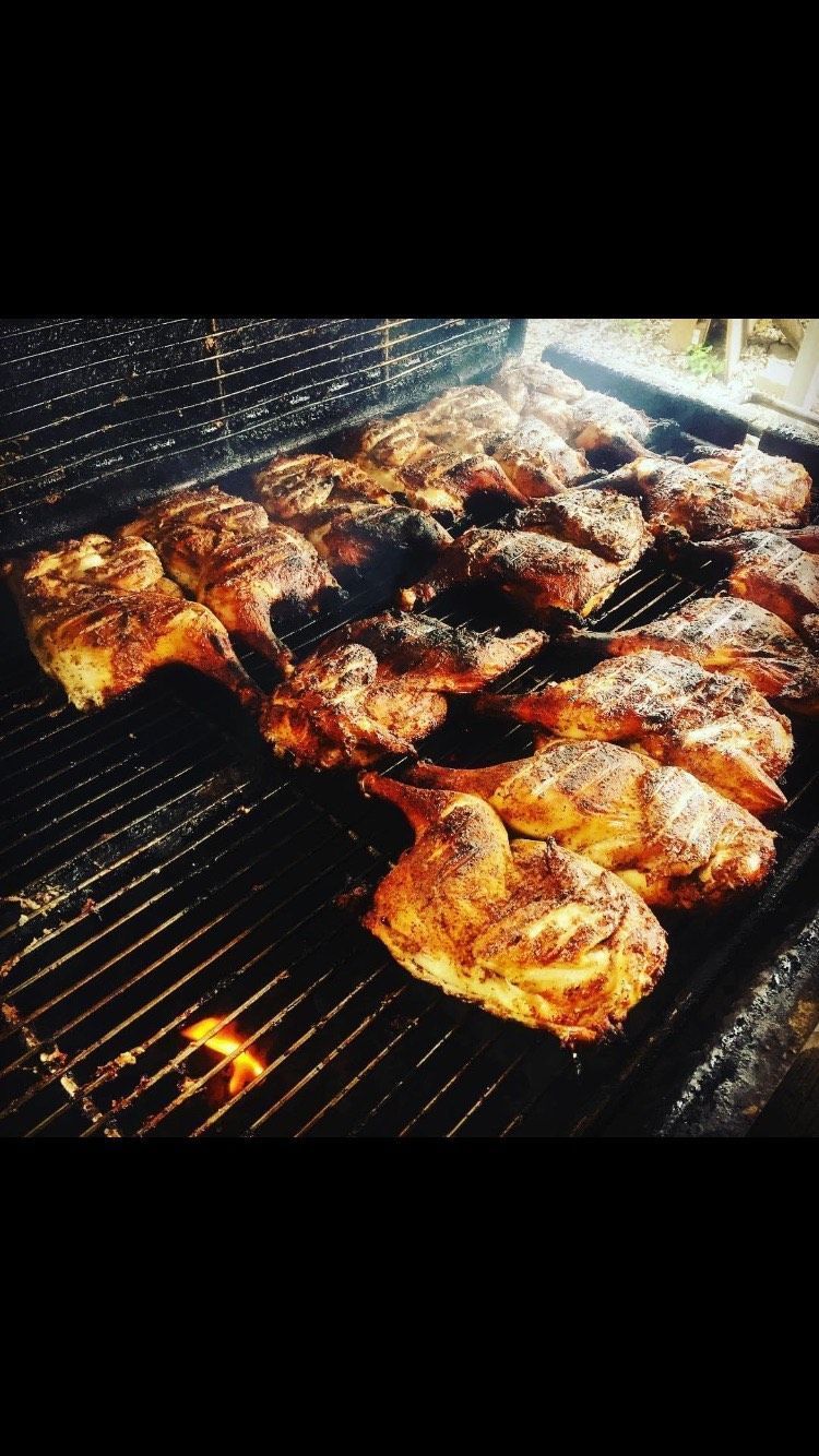 Multiple halves of golden-brown roasted chicken cooking on a large metal grill grate.