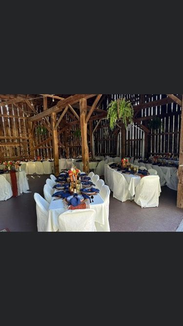 A rustic barn interior set up for a formal event with long tables, white linens, and blue accents.