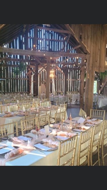 A rustic wooden barn wedding venue set up with long banquet tables, gold chairs, and white linens.