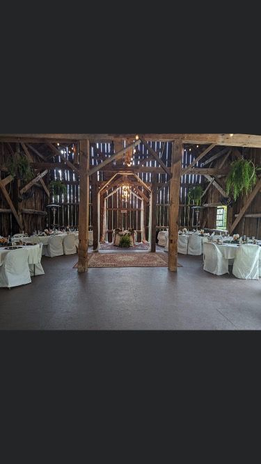 A rustic barn venue set up for a wedding reception with round tables, white linens, and a wooden altar structure.