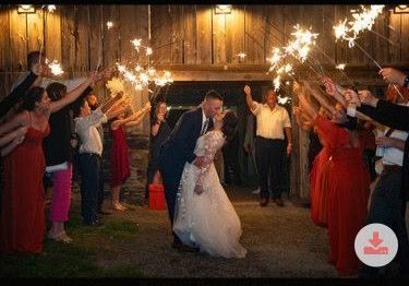 A couple kisses during a sparkler send-off at an evening barn wedding, surrounded by guests holding lit sparklers.