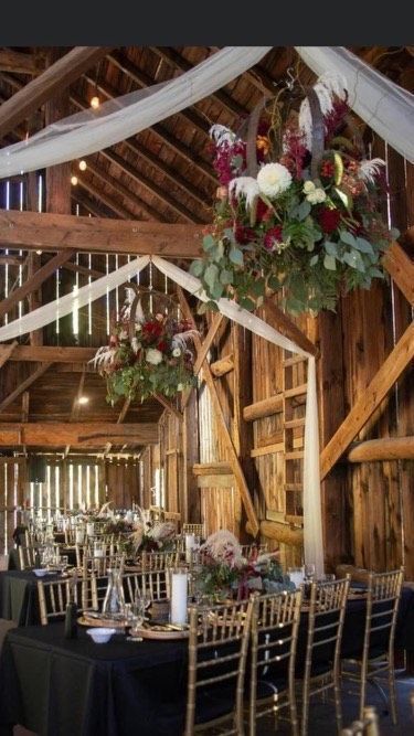 Rustic barn reception with tables set for a meal, featuring hanging wagon wheel floral centerpieces and white drapes.