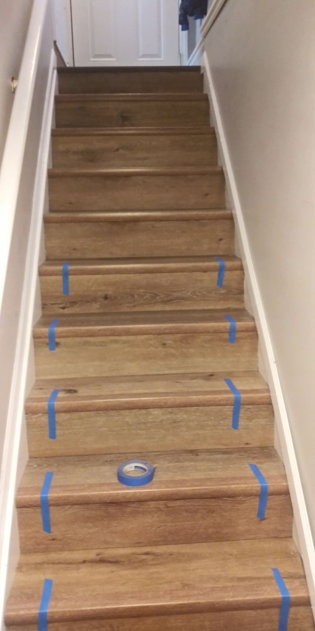 Wooden stairs with blue painter's tape on the steps. A roll of tape rests on one step.