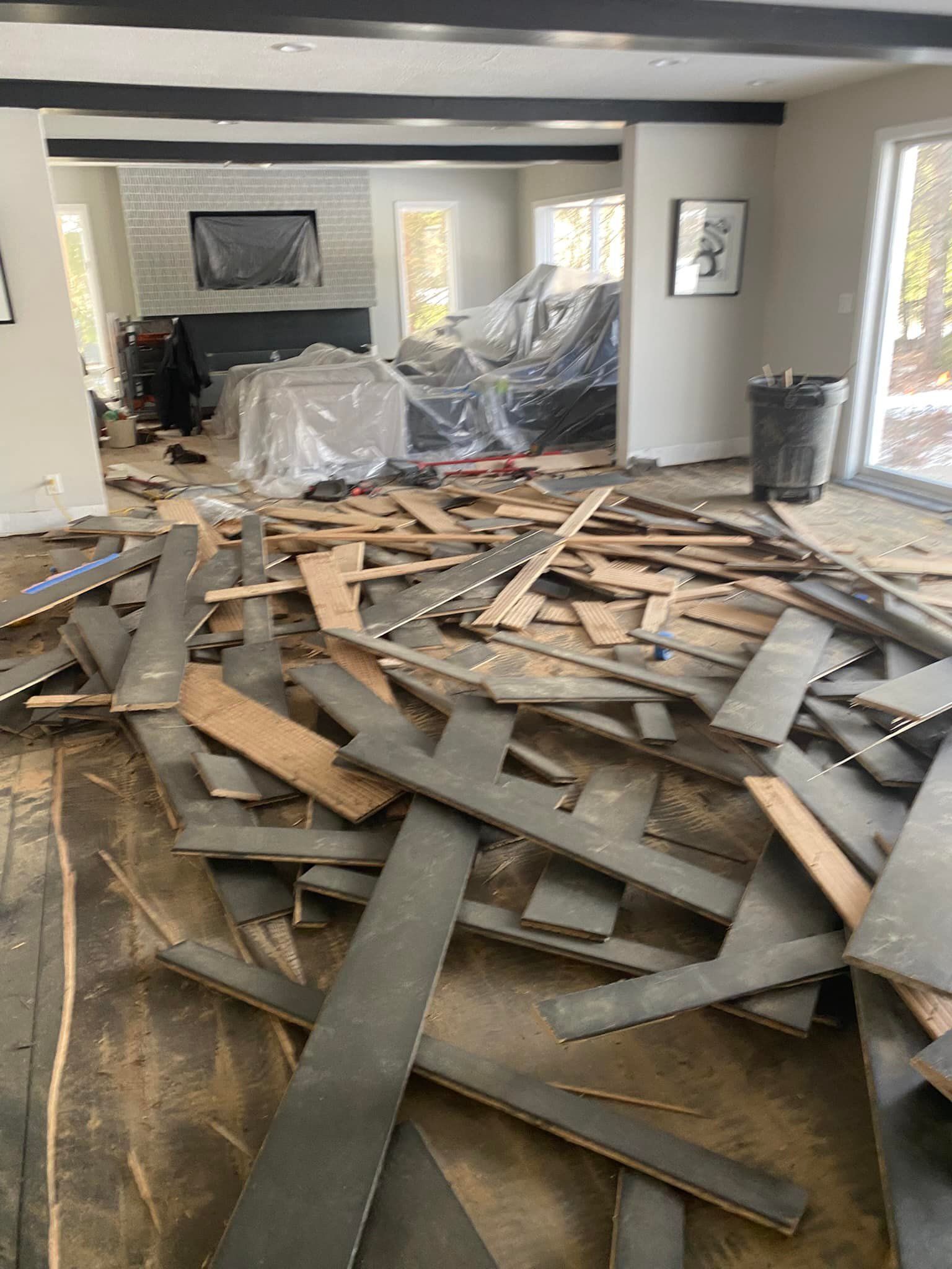 Room undergoing renovation: wood flooring debris scattered across the floor. Furniture covered in plastic.