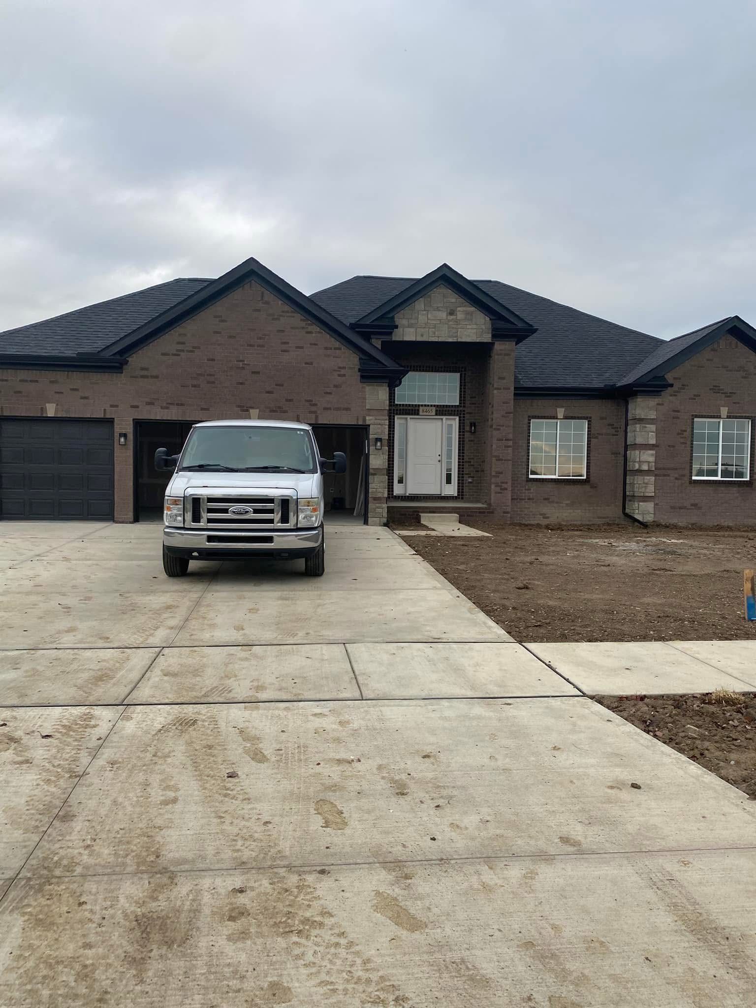 White van parked in front of a brick house under construction. Dark roof, grey sky.