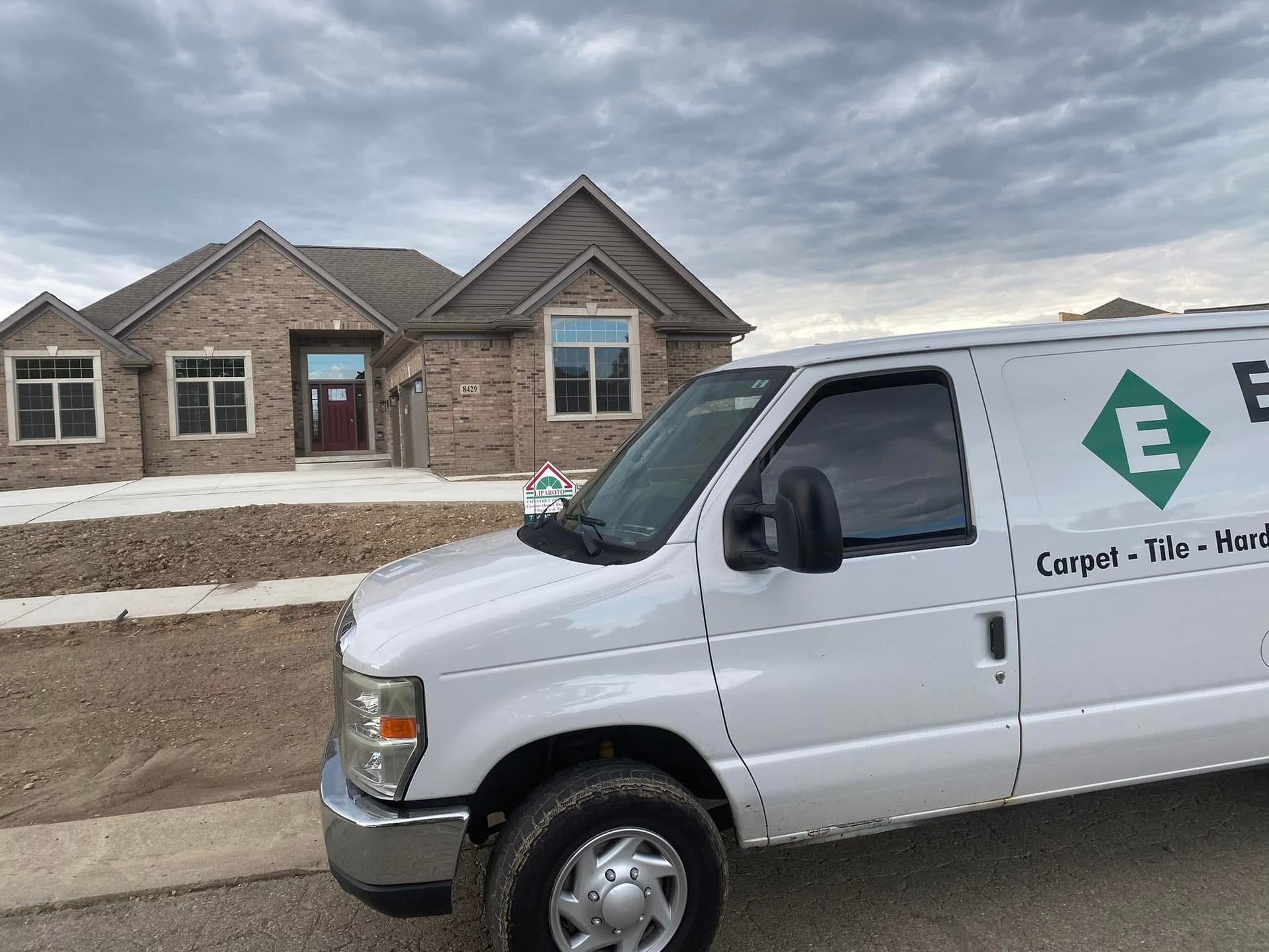 White van with company logo parked in front of a brick house under cloudy sky.