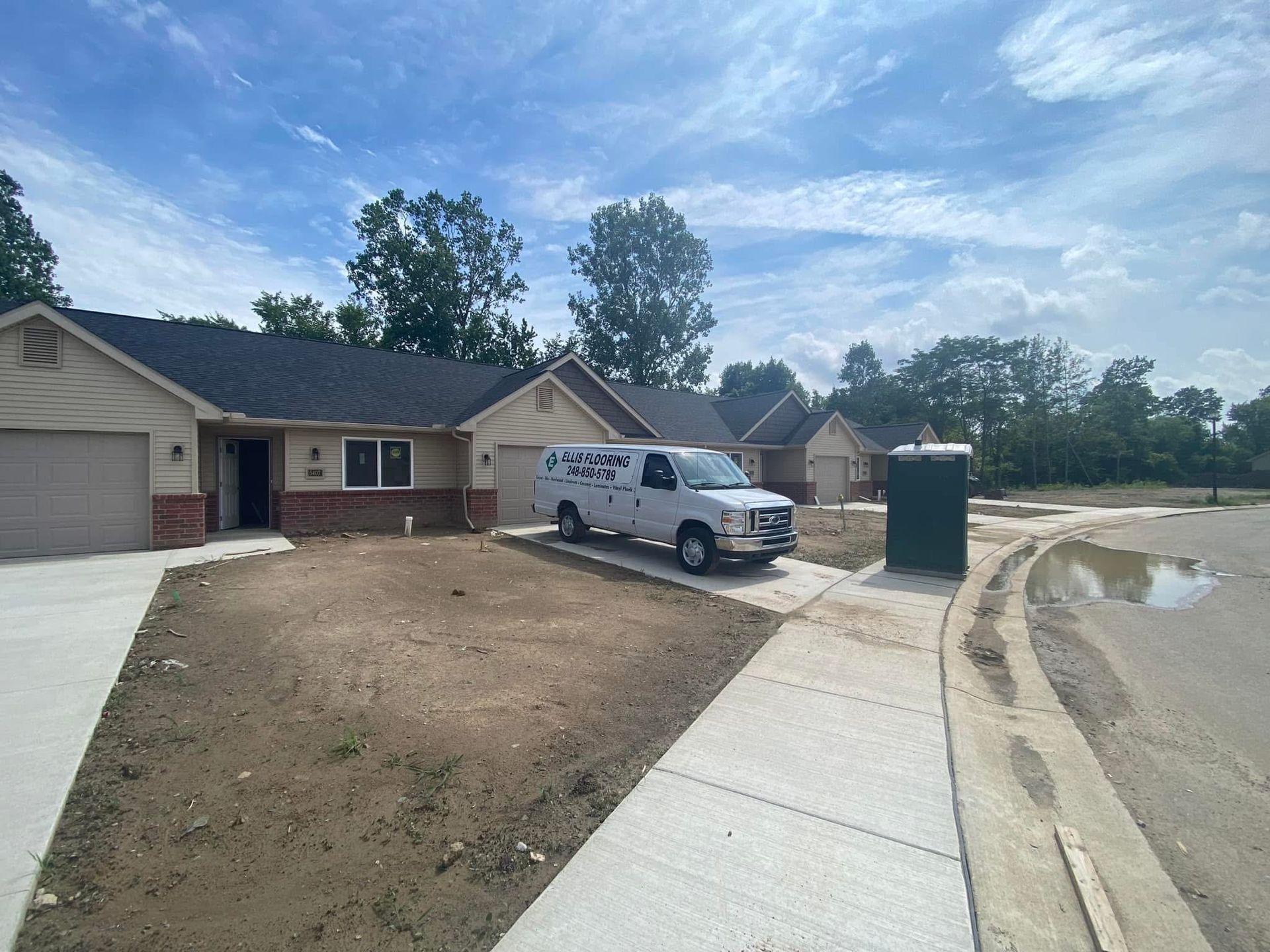 A white van parked in front of newly constructed houses with a portable toilet on the right side.