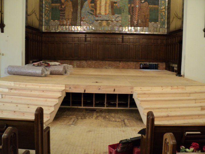 A wooden stage being built in front of a dark wood backdrop, possibly a church interior.