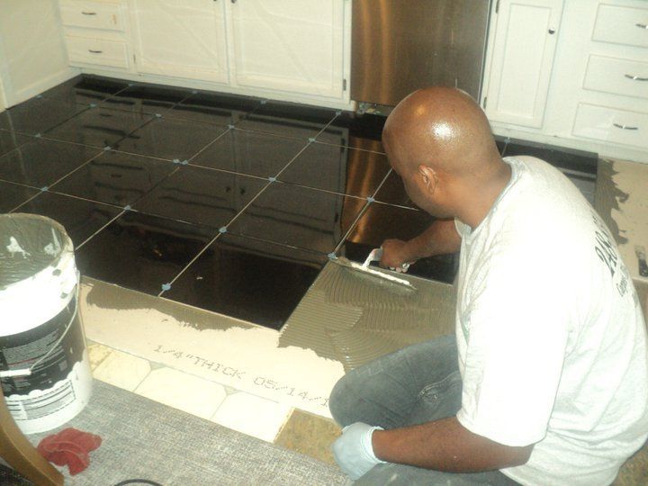 Man tiling a black kitchen floor, applying grout with a trowel.