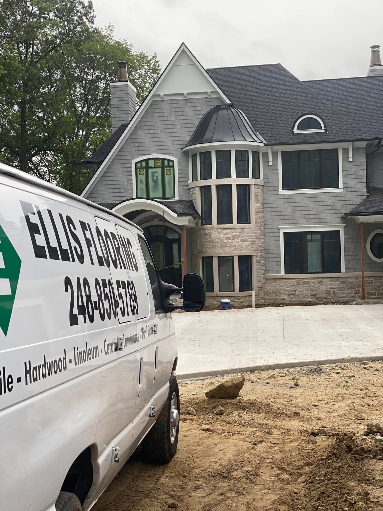 White van parked in front of a gray multi-story house with construction work.