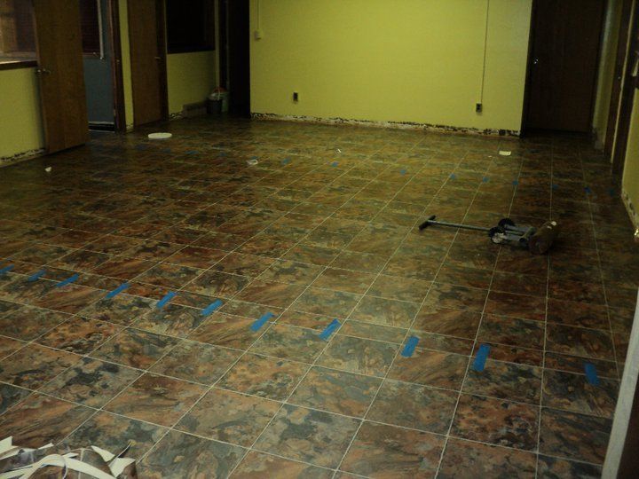 Brown tiled floor in a room, with blue tape and tools, likely renovation in progress.
