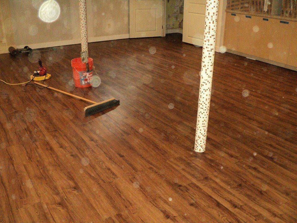 Brown laminate floor with a broom, bucket, and support columns in a room.