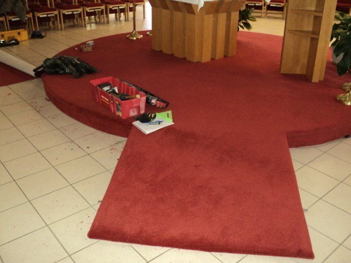 Red carpeted altar area, with tools and supplies, in a church with tile floor.
