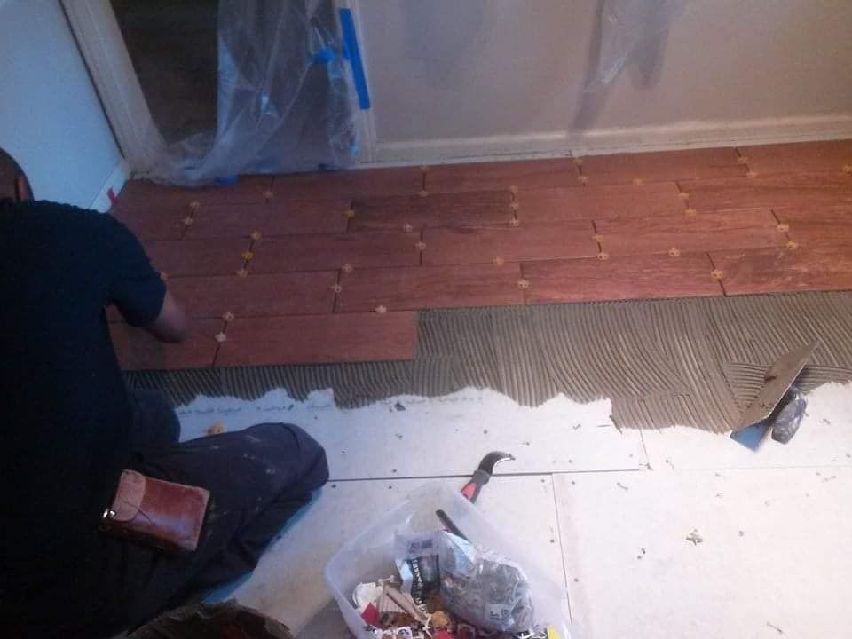 Person installing red wood tile flooring on a white floor, indoor setting.