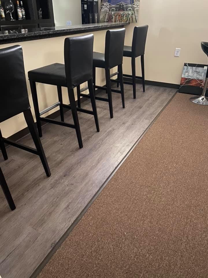 Four black bar stools at a bar with gray flooring next to brown carpet.