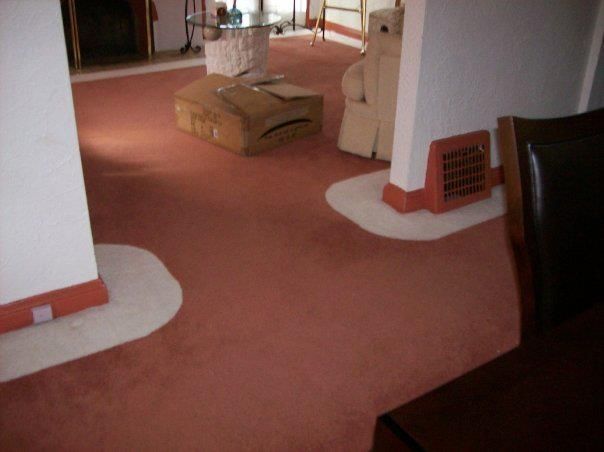 Interior shot of a room with pinkish-red carpet. White support columns and tan furniture are visible.