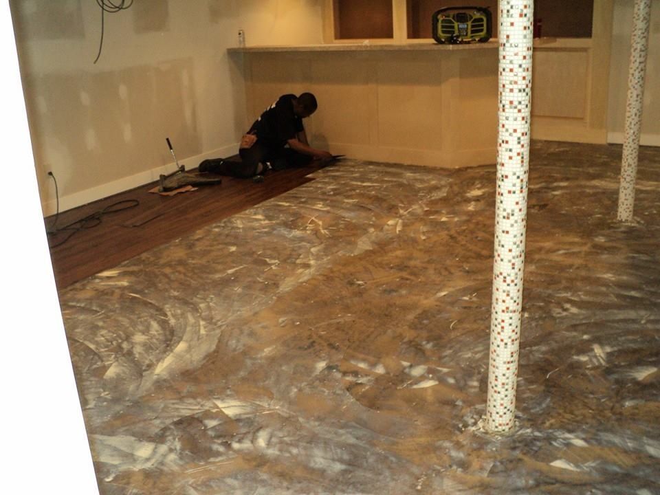Person installing flooring in a basement. Floor has a marbled epoxy finish. Brown and white.