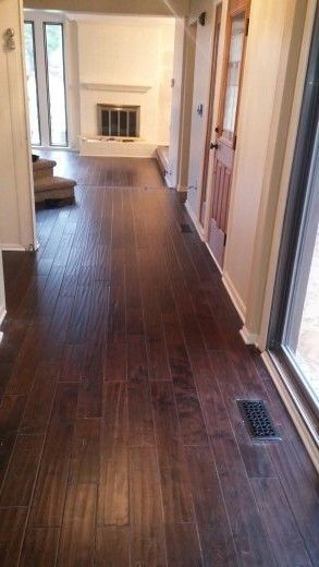 Dark wood floor hallway leading to a fireplace, doorway, and stairs. Sunlight streams in from window.