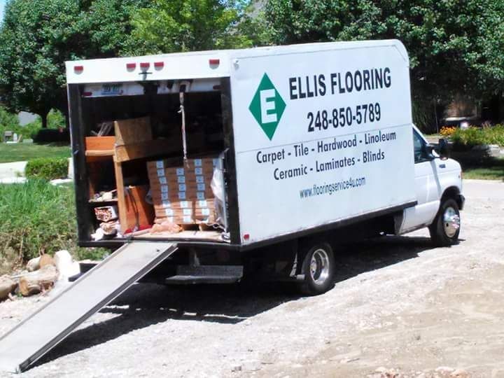 White Ellis Flooring truck with ramp open, parked outdoors with flooring materials loaded.