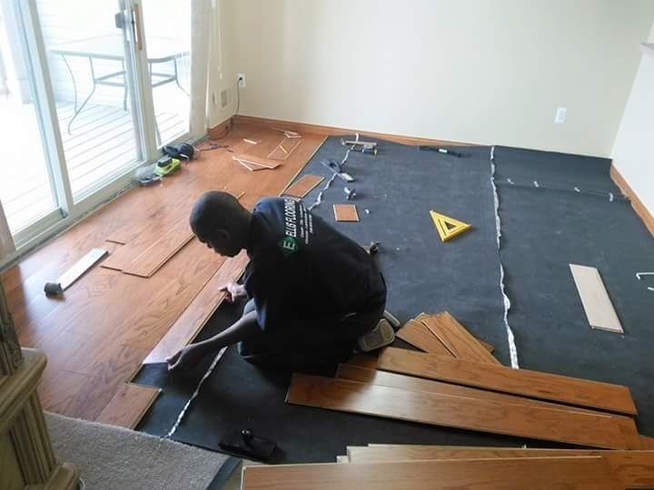 Man installing hardwood flooring in a room with a sliding glass door.