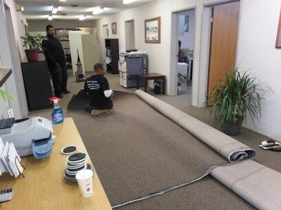 Two men laying out a long rolled carpet in an office.