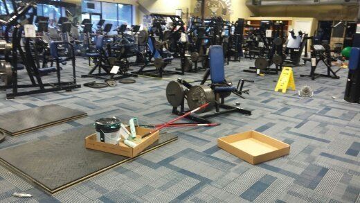 Gym interior with fitness equipment, tools, and safety sign, on a carpeted floor.