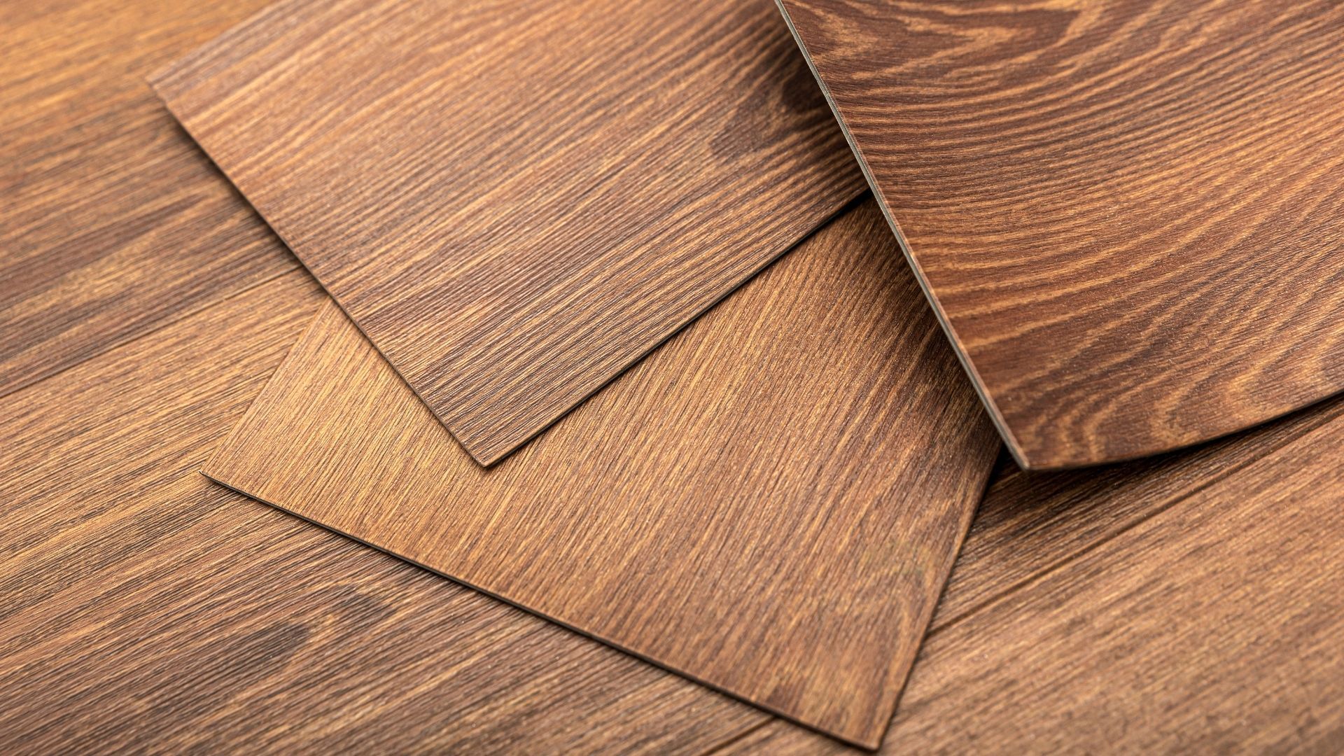 Close-up of brown wood-grain flooring tiles, overlapping and angled, showing detailed texture.