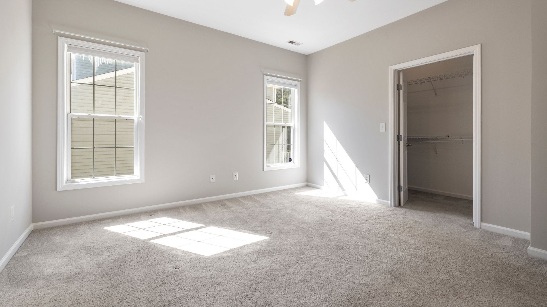 Empty bedroom with gray walls, carpet, two windows, and an open closet.