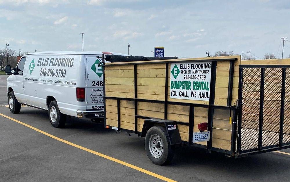 White van with logo towing a trailer with wooden sides and a black wire mesh back. 