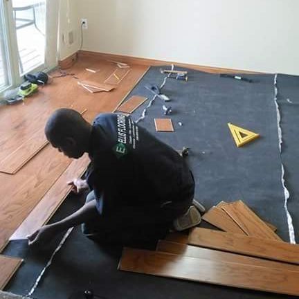 A person installing hardwood flooring in a room. The person is kneeling, working on the planks.