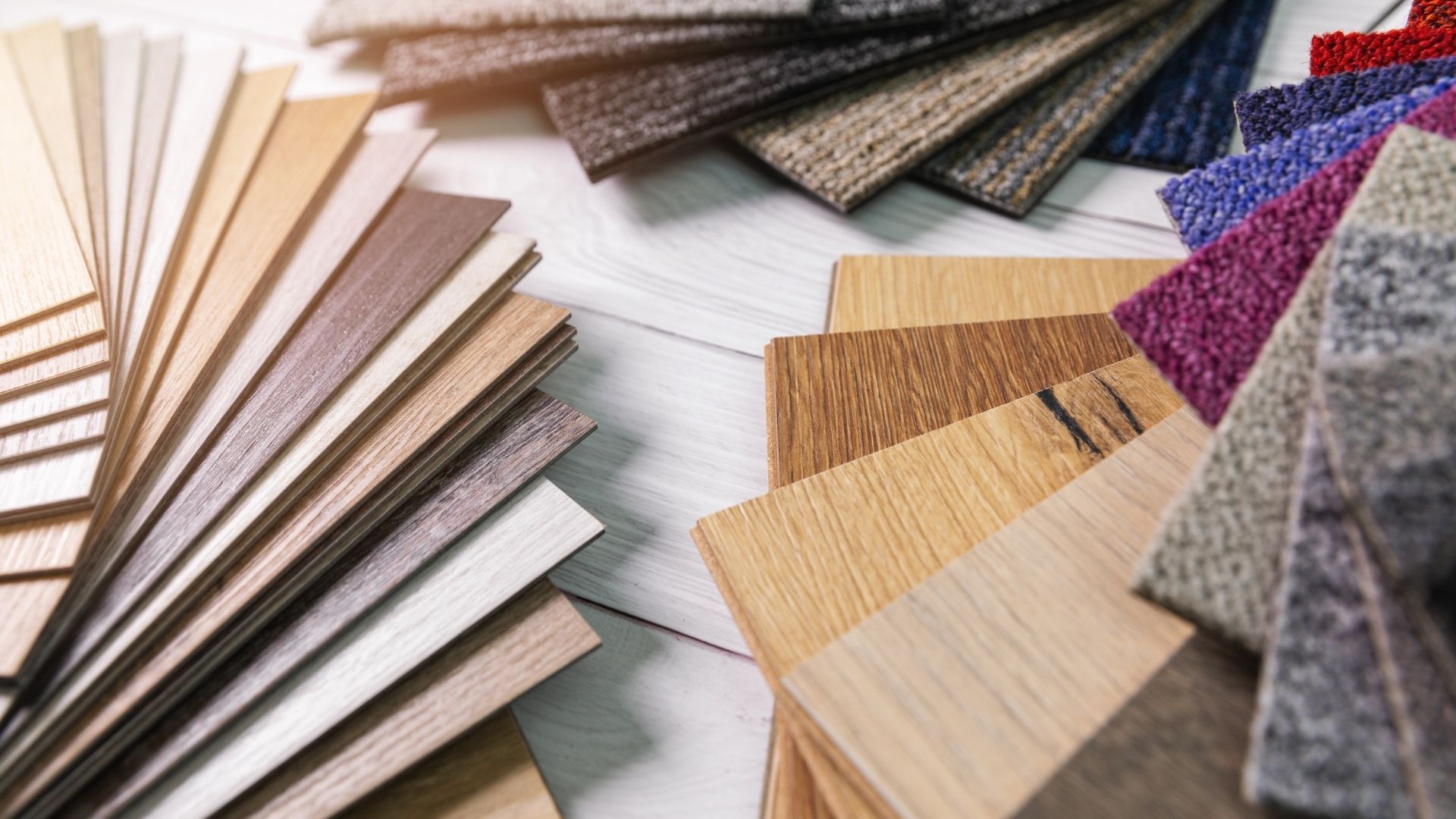 Various flooring samples fanned out, showcasing wood, carpet, and other textures in a variety of colors on a light-colored surface.