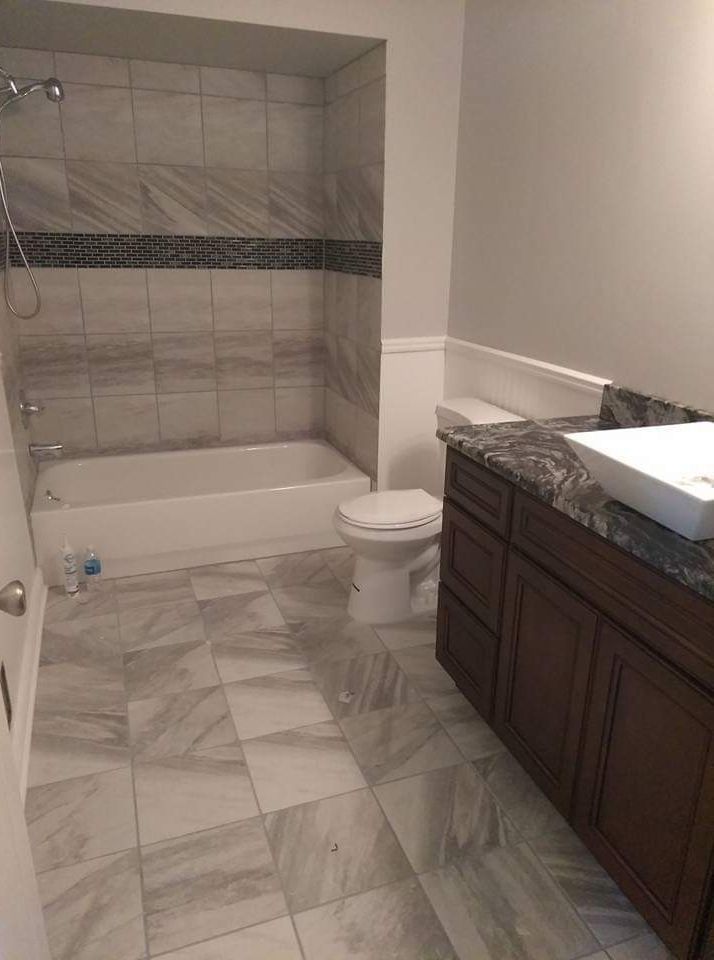 Bathroom with marble tile, bathtub, toilet, dark wood vanity, and white countertop.