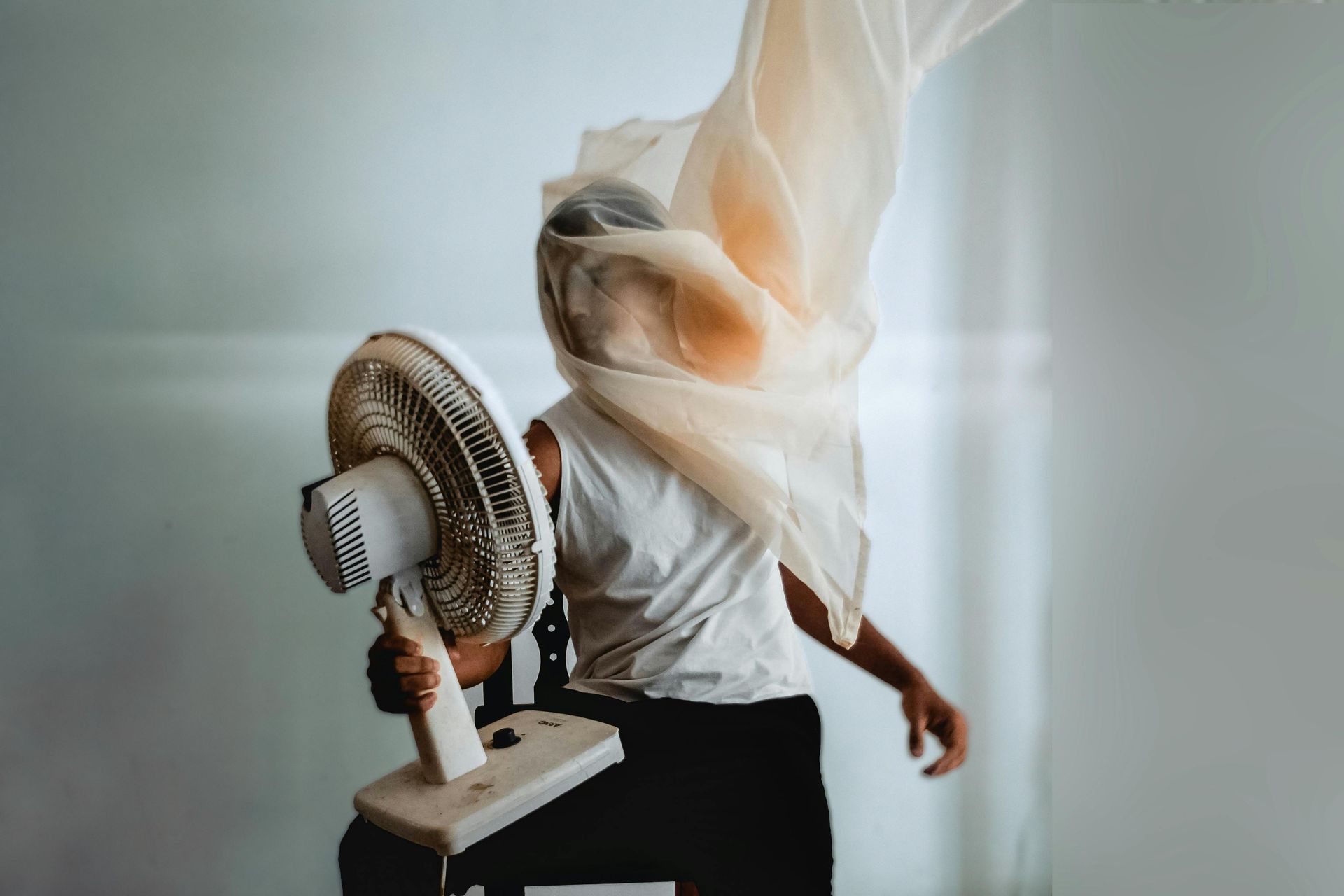 A man is covering his face with a scarf while holding a fan.