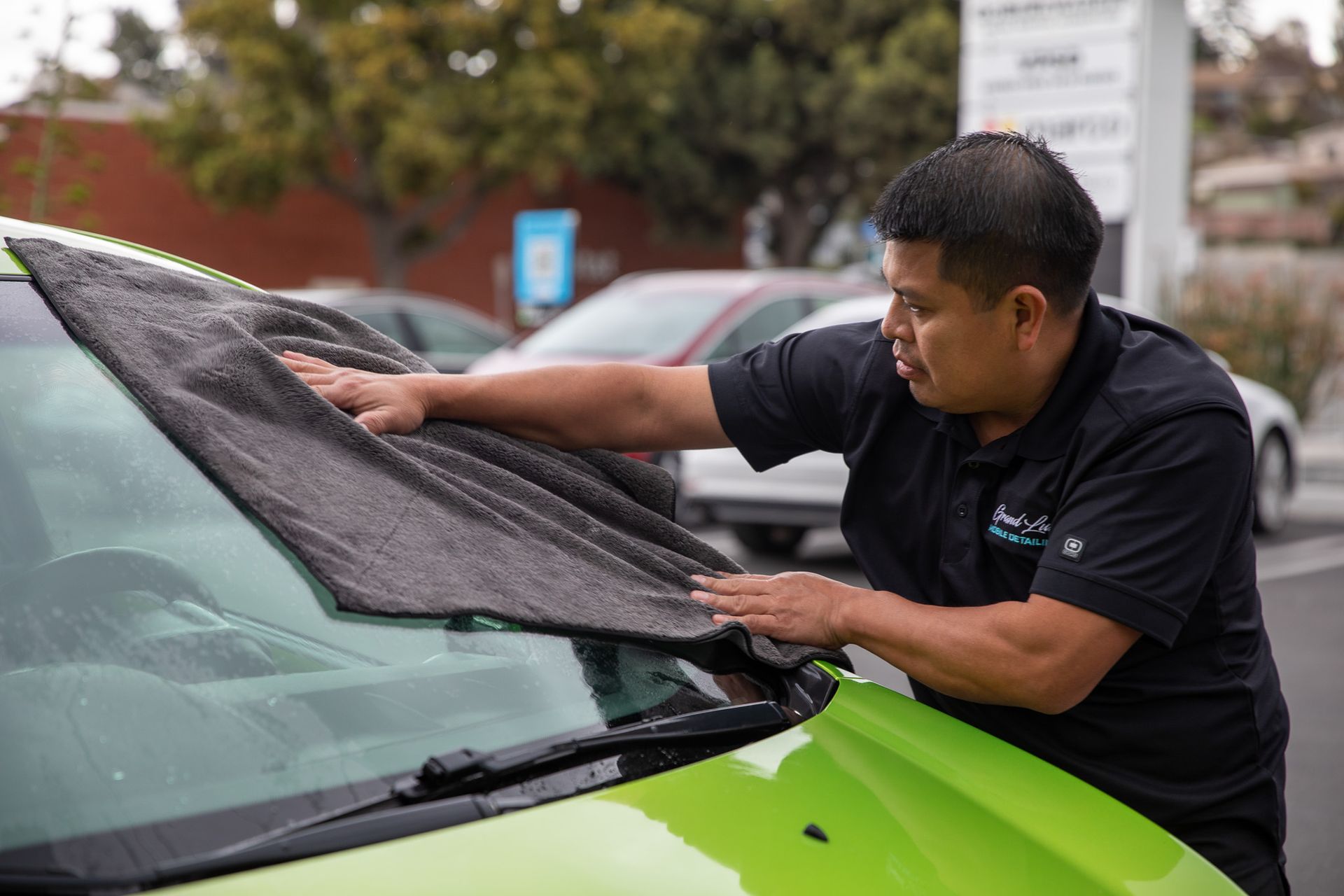 A man is cleaning the windshield of a green car with a towel.