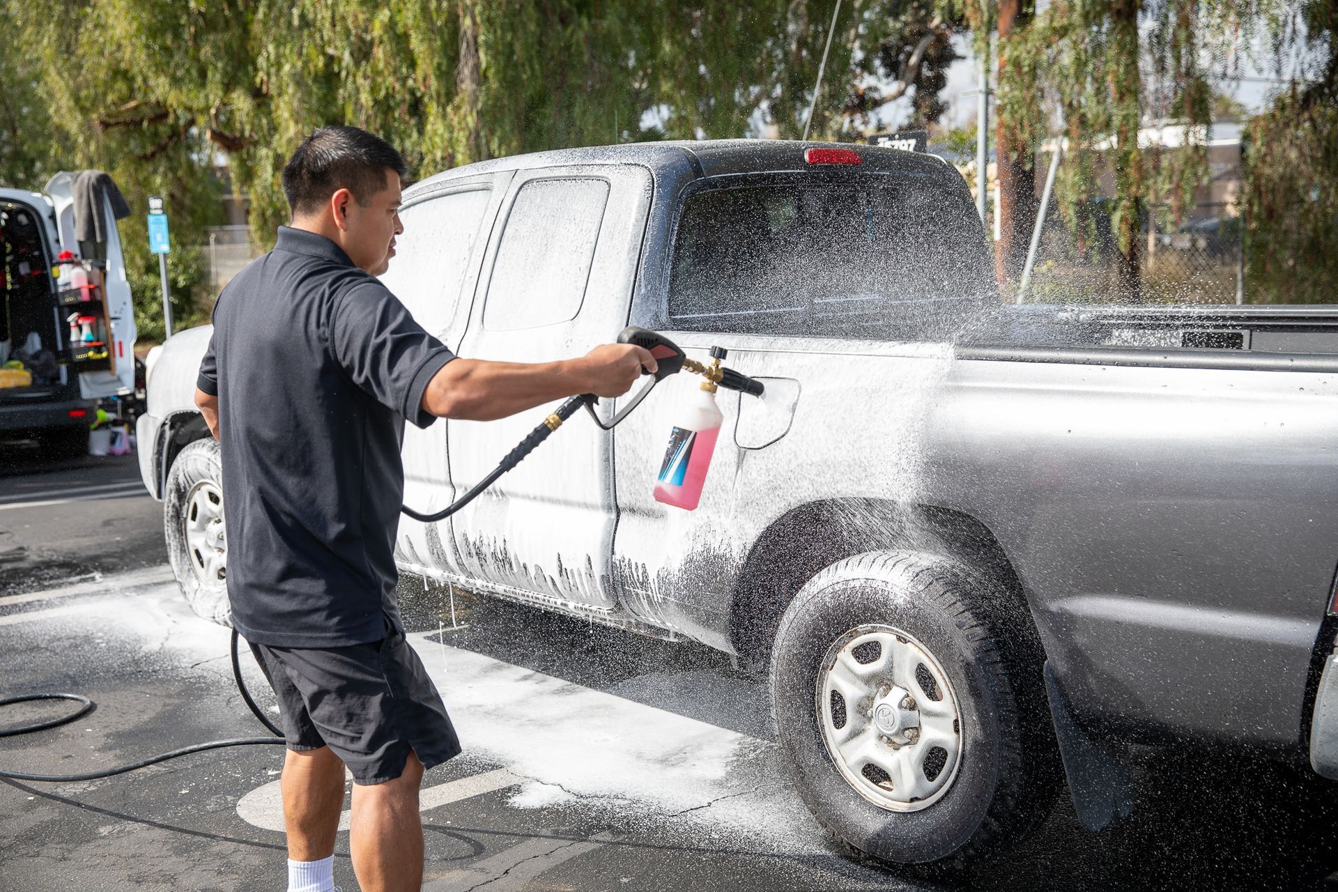 A man is washing a truck with a high pressure washer.