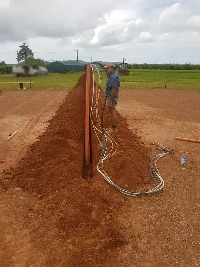 Man Installing Electrical Wires in a Brown Dirt Trench. Outdoor Setting, Cloudy Sky — Ionspark Electrical in Atherton, QLD