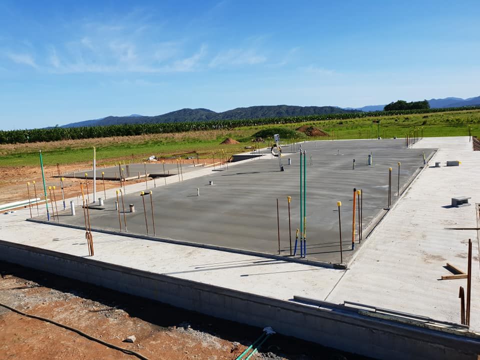 Concrete foundation poured for a building in a rural setting, plumbing pipes visible, clear sky.— Ionspark Electrical in Atherton, QLD