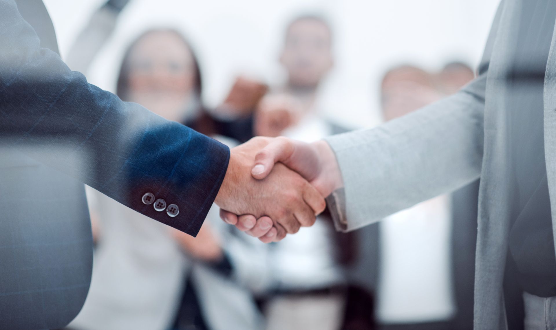 Two people in suits shaking hands, business deal, blurred background.