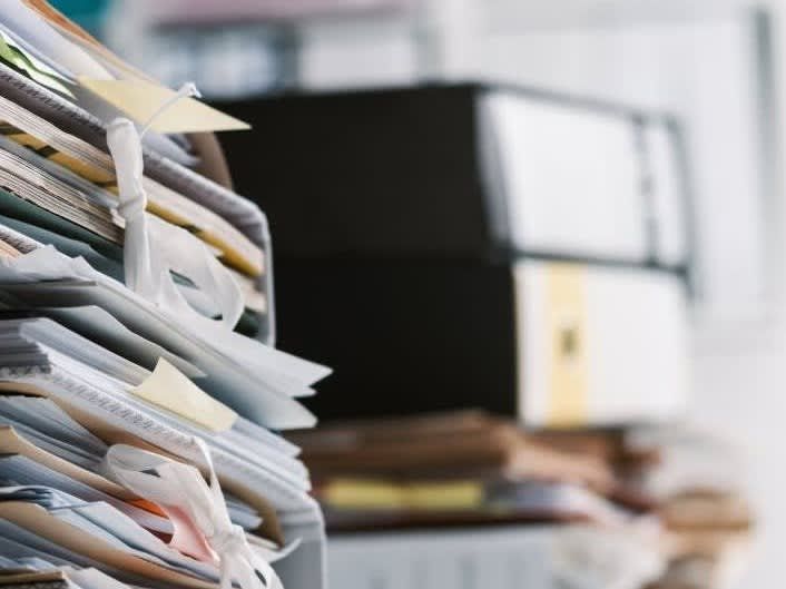 Pile of papers and binders in an office setting, suggesting a cluttered workspace or document storage.