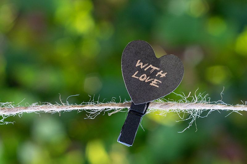 A black heart with the words `` with love '' written on it is hanging on a rope.