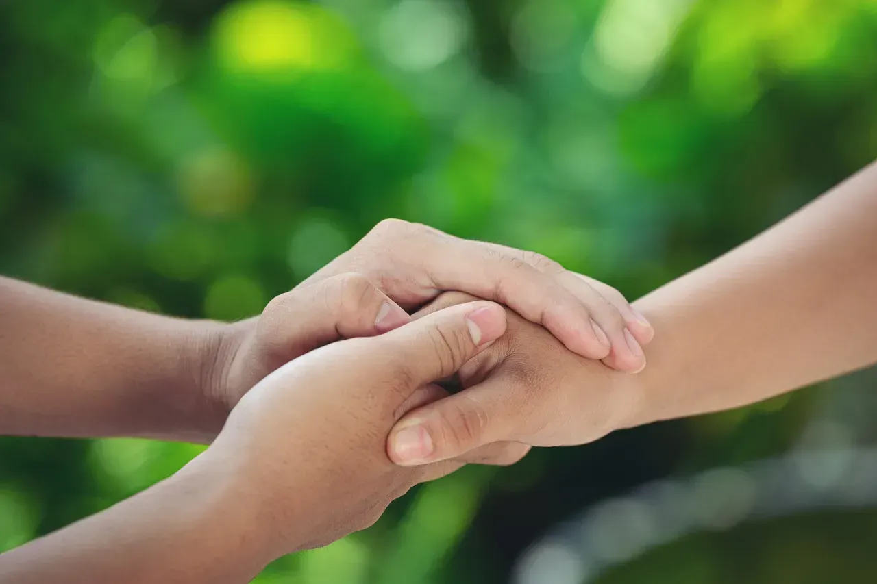 A close up of two people holding hands with a green background.