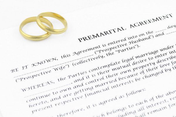 Two gold wedding rings on top of a premarital agreement