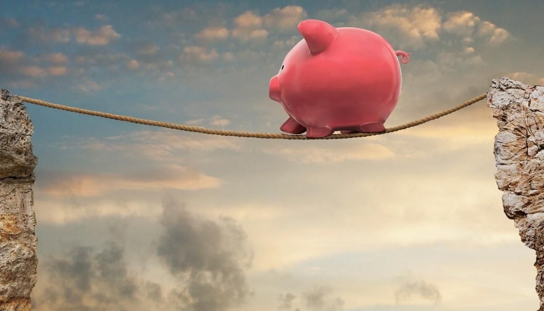 A pink piggy bank is standing on a rope over a gap.