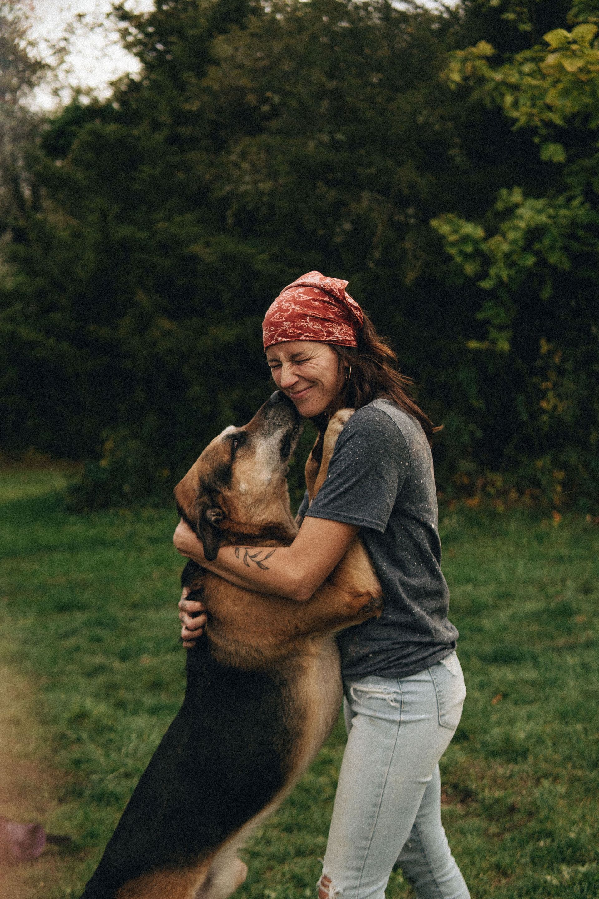 Woman with red bandana hugs a German Shepherd outdoors on green grass.