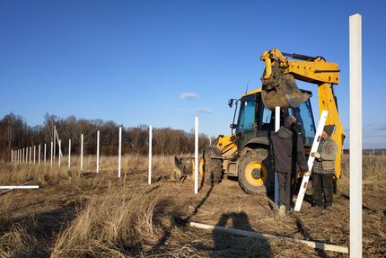 The excavator with the bucket clogs the iron pillars for the fence in the field
