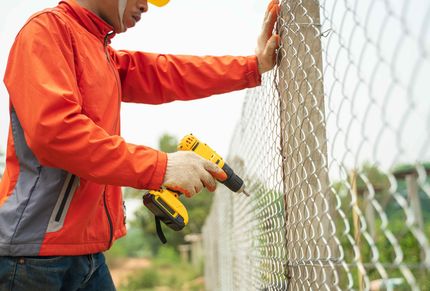 Installing wire mesh fence with screws drill at farm