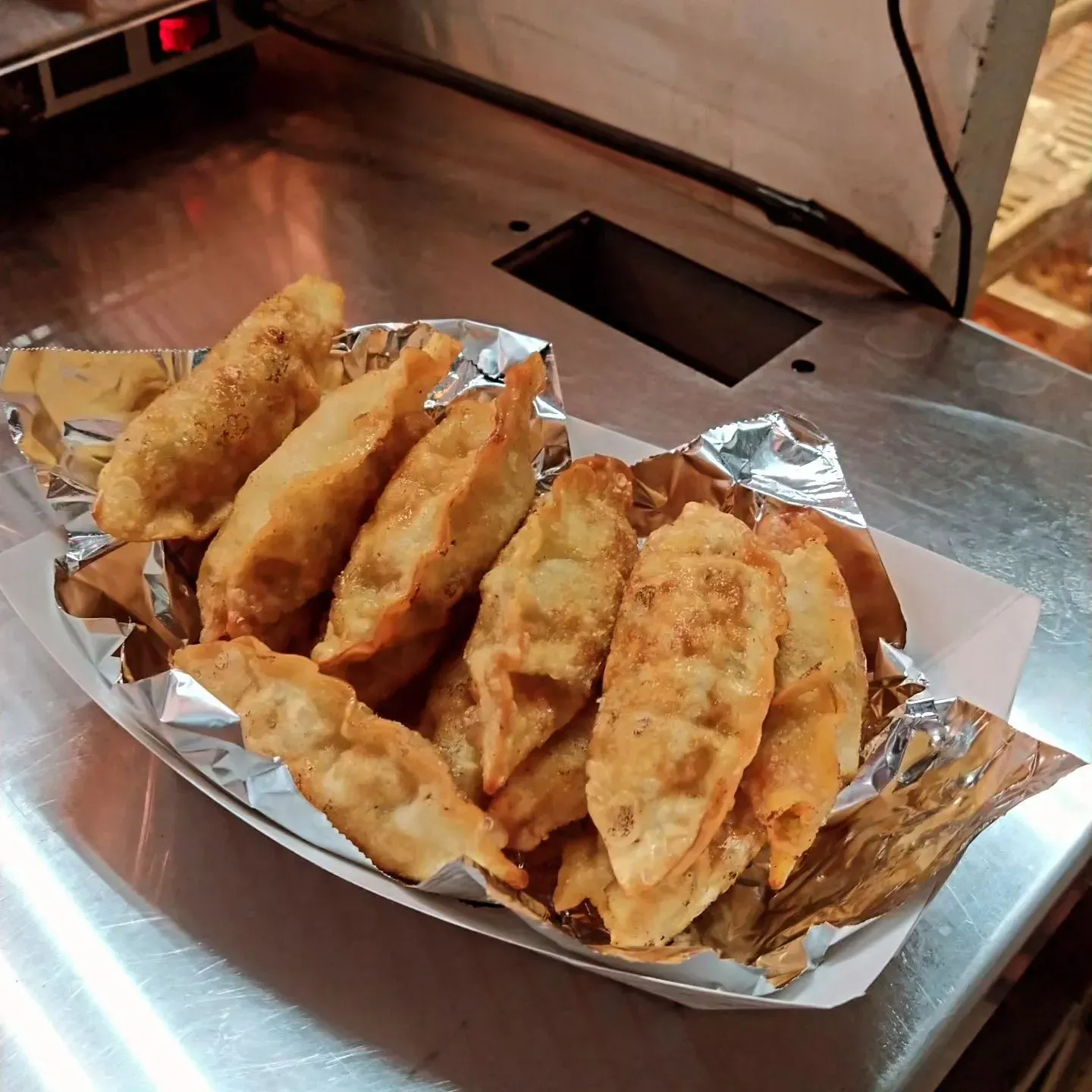 Fried dumplings in a foil-lined paper tray on a stainless steel counter.