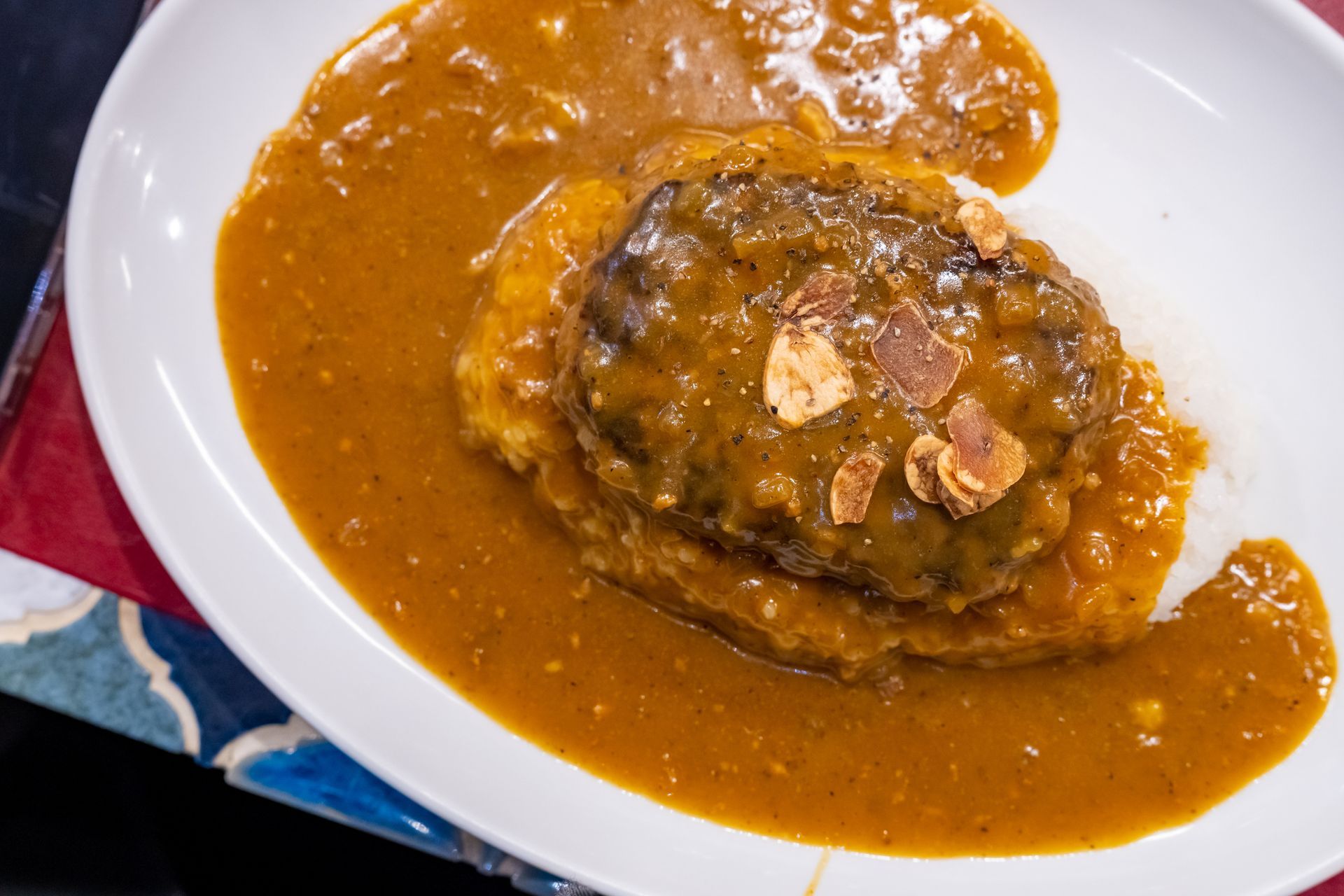Hamburger steak with sauce and almonds on a bed of rice and curry on a white plate.