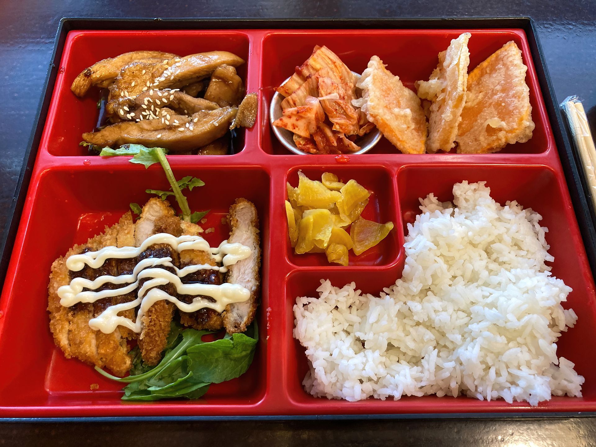 Bento box with fried pork, kimchi, rice, and pickled vegetables.